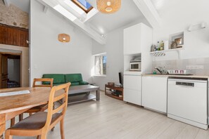 A modern kitchen with white cabinetry, a dining area with a wooden table and chairs, a green sofa, and a skylight.
