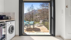 Uma cozinha moderna com máquina de lavar, área de refeições com cadeiras e vista para um pátio com mesa e cadeiras.