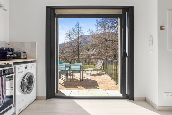 A modern kitchen with a washing machine, a dining area with chairs, and a view of a patio with a table and chairs.