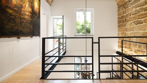 Un interior con techo alto, paredes de ladrillo visto, un cuadro grande a la izquierda y una escalera con barandillas negras.