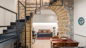 Un interior moderno con un arco de piedra que conduce a una sala de estar, una escalera con barandillas de metal y una mesa de comedor con sillas.