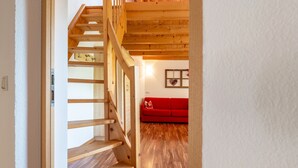A wooden staircase leading to a red sofa in a room with wooden flooring and a white wall.