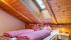 A wooden cabin room with a skylight, a bed with red and white checkered bedding, and a bedside table with a lamp.