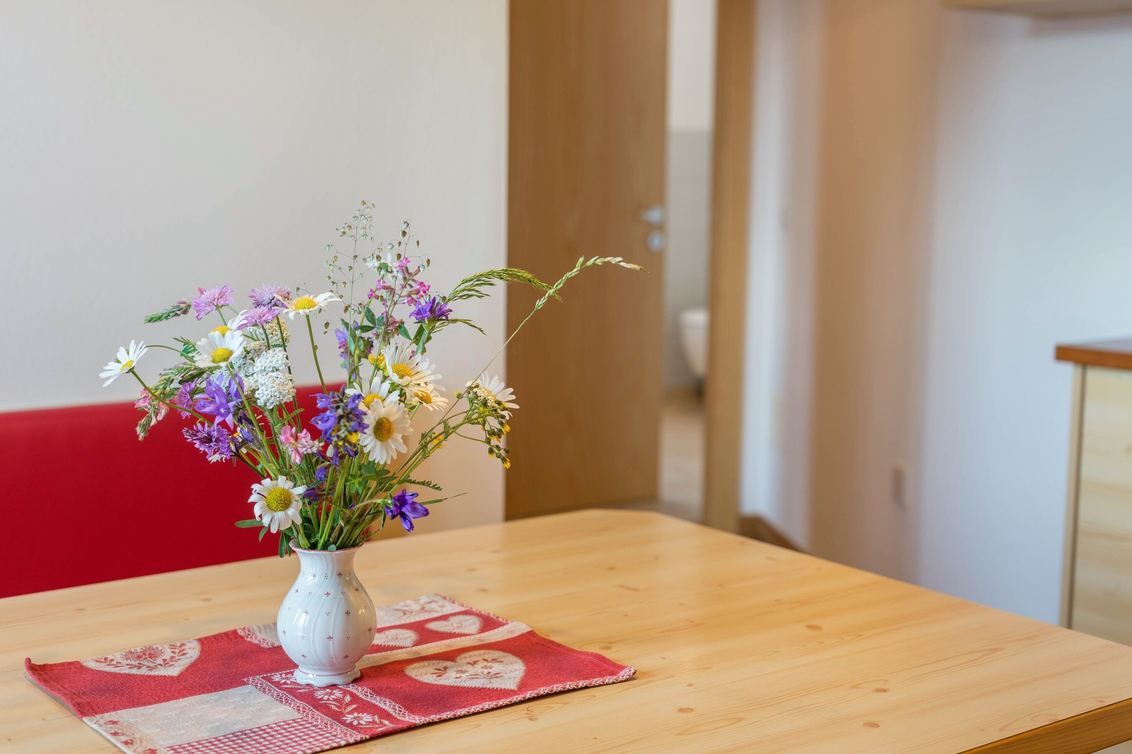 A wooden table with a white vase containing a variety of flowers.