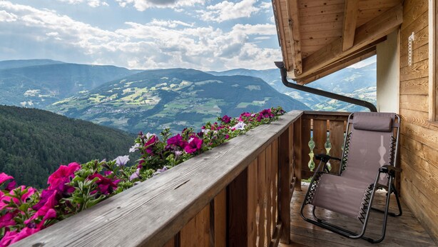 Een houten balkon met uitzicht op bergen, een ligstoel en een houten leuning.
