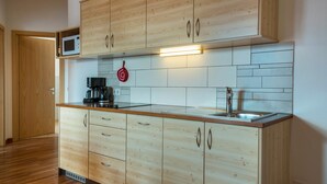 Een keuken met houten kastjes, een magnetron, een koffiezetapparaat en een spoelbak.