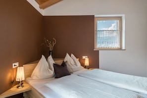 A bedroom with a bed, pillows, bedside lamps, a window with a view, and a vase with branches.