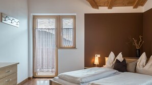 Een slaapkamer met een bed, een nachtkastje met een lamp, een raam met gordijnen en een houten dressoir.