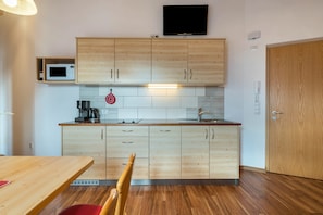 A modern kitchen with wooden cabinets, a microwave, a coffee maker, and a TV mounted above the cabinets.