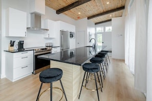 A modern kitchen with white cabinets, a stainless steel refrigerator, a black countertop, and a wooden ceiling.