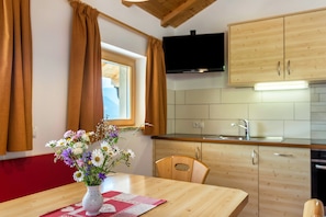 A kitchen with wooden cabinets, a TV mounted above the counter, and a window with curtains.