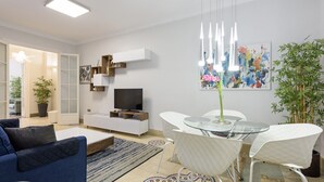A modern living room with a sofa, TV, glass table, chairs, and artwork on the wall.