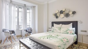 A hotel room with a bed, two chairs, a small table, and a decorative wall piece.