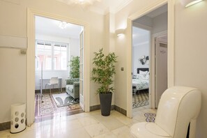 Un pasillo con una planta en maceta, una silla blanca y una cama al fondo.