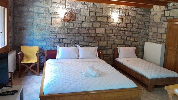 Une chambre avec deux lits, un mur en pierre, des poutres en bois au plafond, une chaise et un téléviseur.