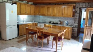 Une cuisine avec des meubles en bois, un plan de travail en granit, une table à manger avec des chaises et un réfrigérateur.