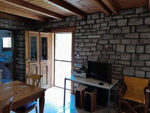 Una habitación con paredes de piedra, una mesa de madera para comer, sillas, un televisor y altavoces.