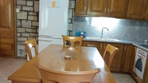 Une table à manger en bois avec des chaises, un mur en pierre, un réfrigérateur et des meubles de rangement en bois dans un coin cuisine.