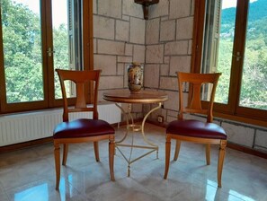 A room with two wooden chairs with red cushions, a round table, and a vase on the table.
