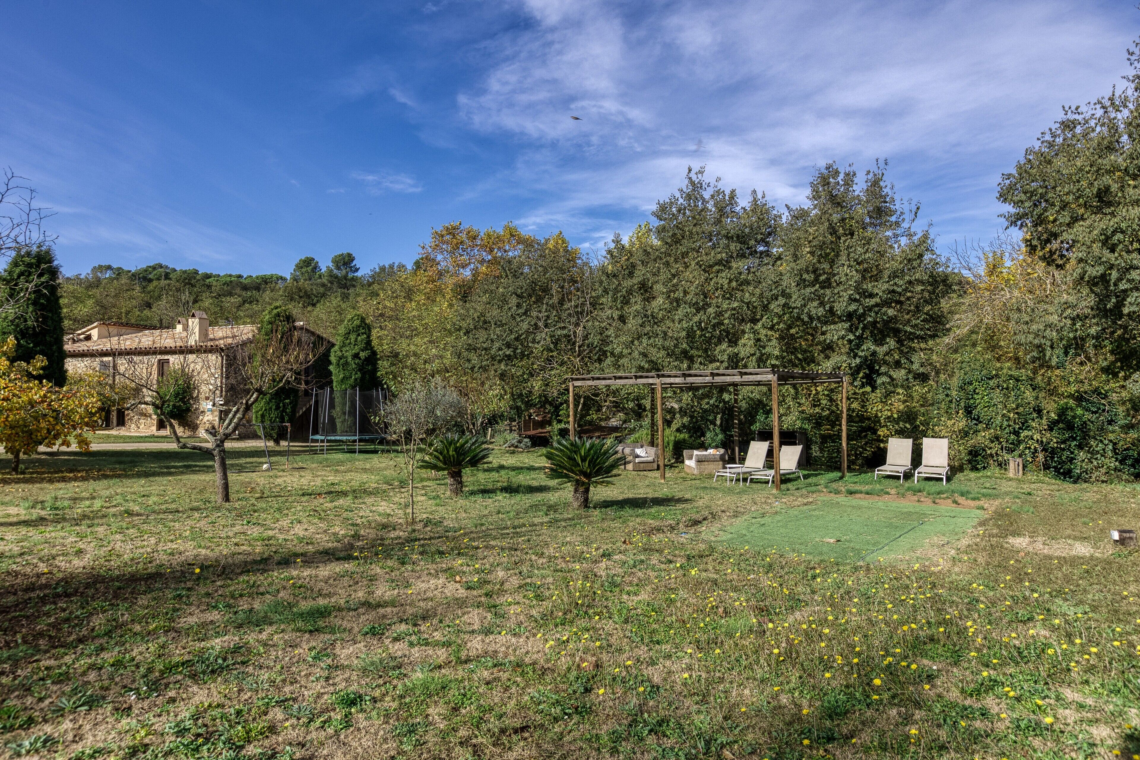 A garden with a pergola, outdoor seating, and a house in the background.