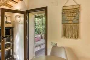 Une pièce avec une porte vitrée donnant sur un balcon, une décoration murale en macramé, une horloge ronde fixée au mur et une chaise blanche.