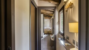 A hallway with a bench, a lamp, and a bed in the distance.