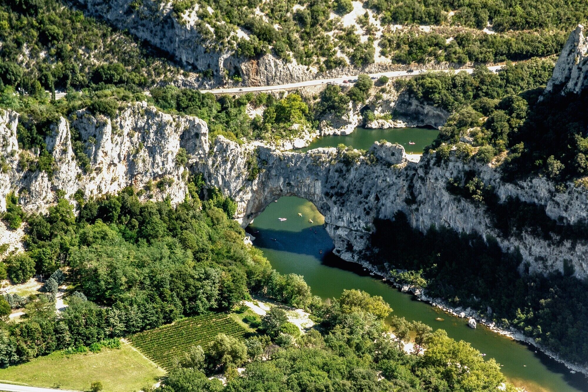 Eine gebirgige Landschaft mit einem Fluss, einer Brücke und einem Weinberg.