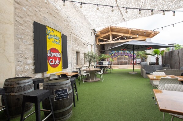 Un patio al aire libre con mesas, sillas y barriles, con un letrero de 'Havana Club' y una estructura de pérgola de madera.