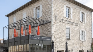 Een gebouw van steen met een balkon, een bordje waarop 'LE TERMINUS' staat, en een bord dat een restaurant-bar aangeeft.
