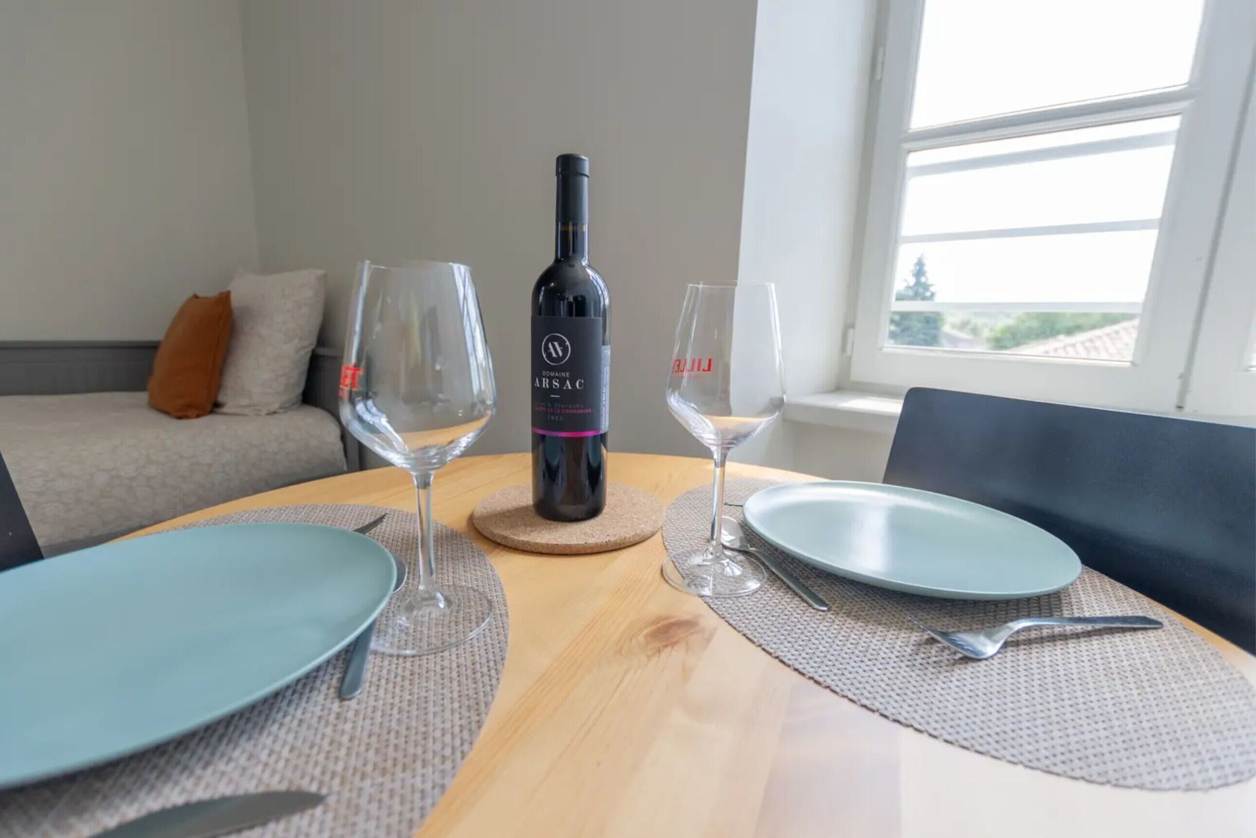 A dining table with a bottle of wine, glasses, plates, and cutlery.
