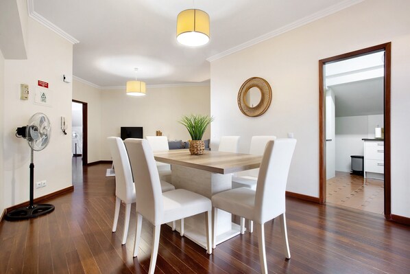 A dining area with a wooden table, white chairs, a fan, and a decorative plant.