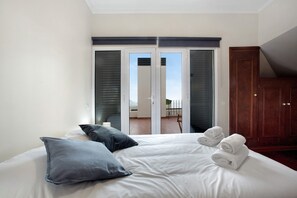 A hotel room with a bed, pillows, a wooden wardrobe, and a sliding glass door leading to a balcony. - Apartment 'Vista Mar' with Sea View, Private Terrace and Wi-Fi (Funchal)