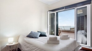 Habitación de hotel con cama, mesita de noche con lámpara, balcón con vistas y puerta corrediza de vidrio.