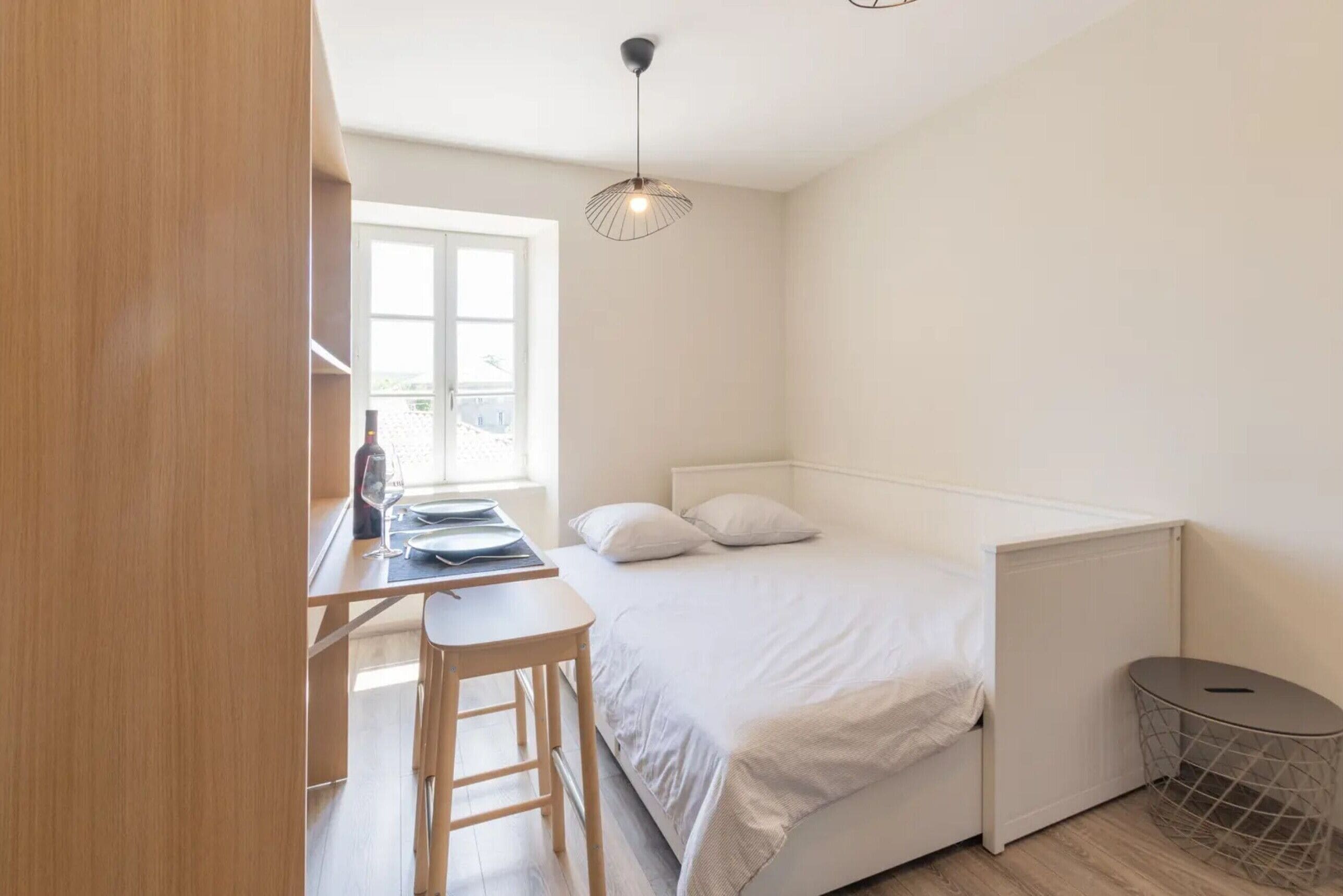 A bedroom with a bed, a desk, and a chair, a window, and a radiator.