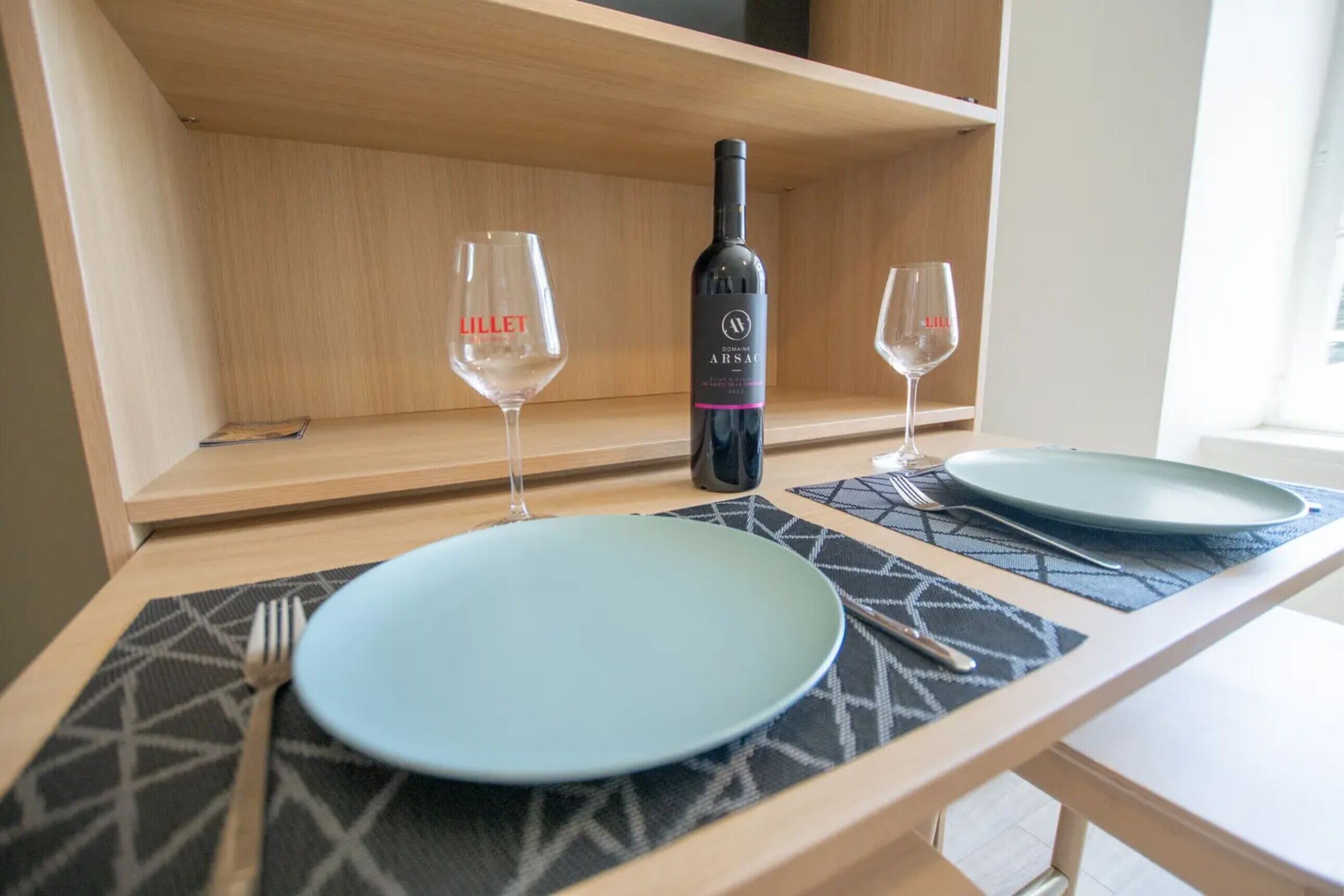 A dining table with two plates, a bottle of wine, and two glasses.