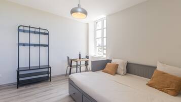 A bedroom with a bed, a desk, a chair, a metal rack, and a window.
