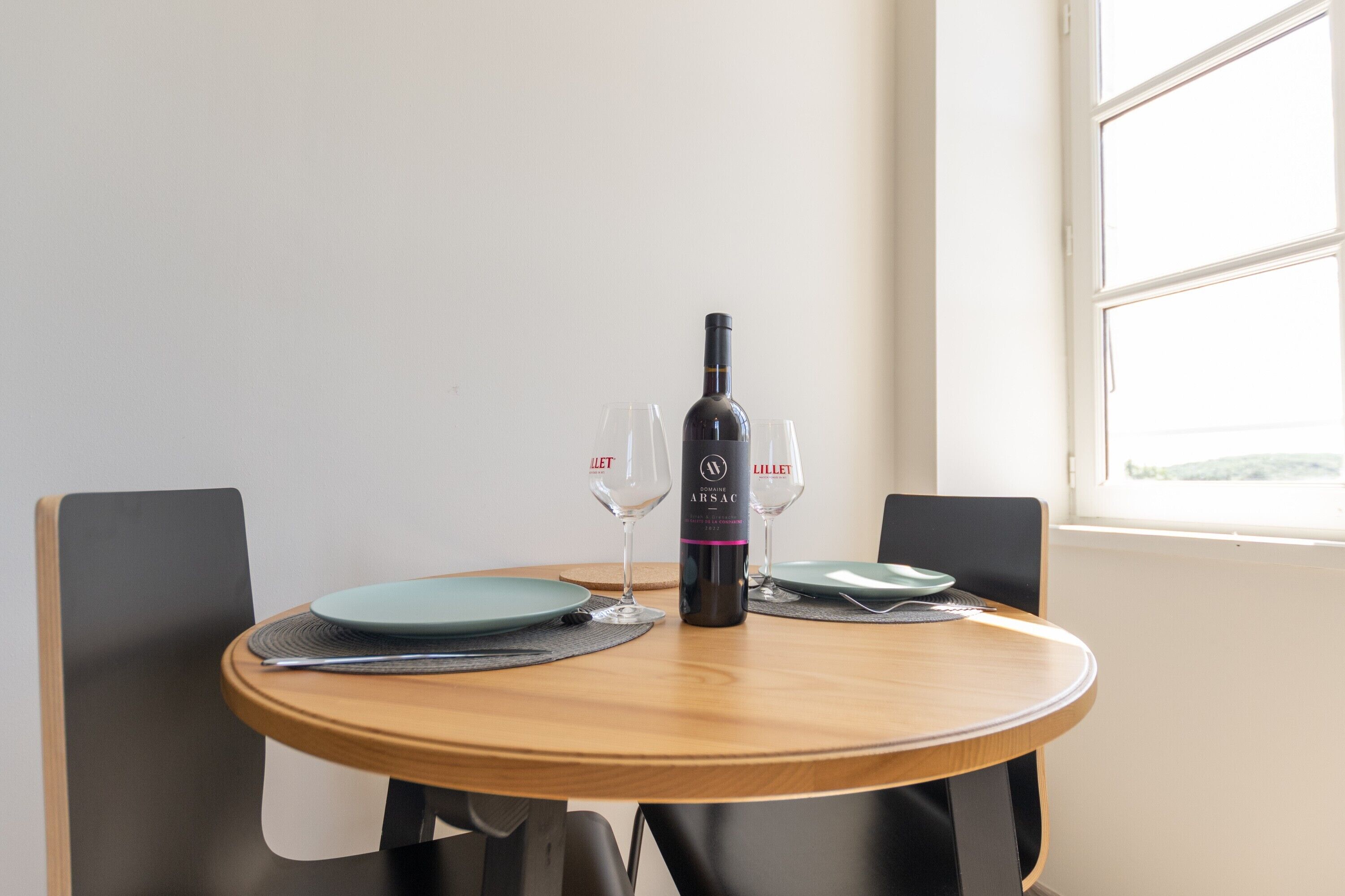 A round wooden table with a bottle of wine, two wine glasses, and plates.
