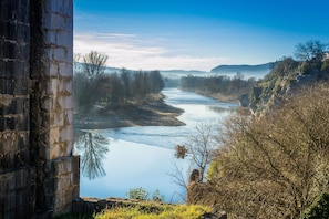 A river with a stone bridge, trees, and a hill with a building. - Apartment In A Hotel 'Chatus' with Wi-Fi and Air Conditioning (Ruoms)