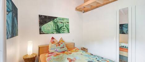 Un dormitorio con cama, una mesita de noche con lámpara, un cuadro en la pared y una viga de techo de madera.