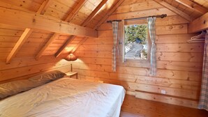 A wooden cabin bedroom with a bed, a window with curtains, and a sloped ceiling. - Chalet "Maison De Bois Finlandaise" with 2 Private Terraces & Balcony (Bolquère)