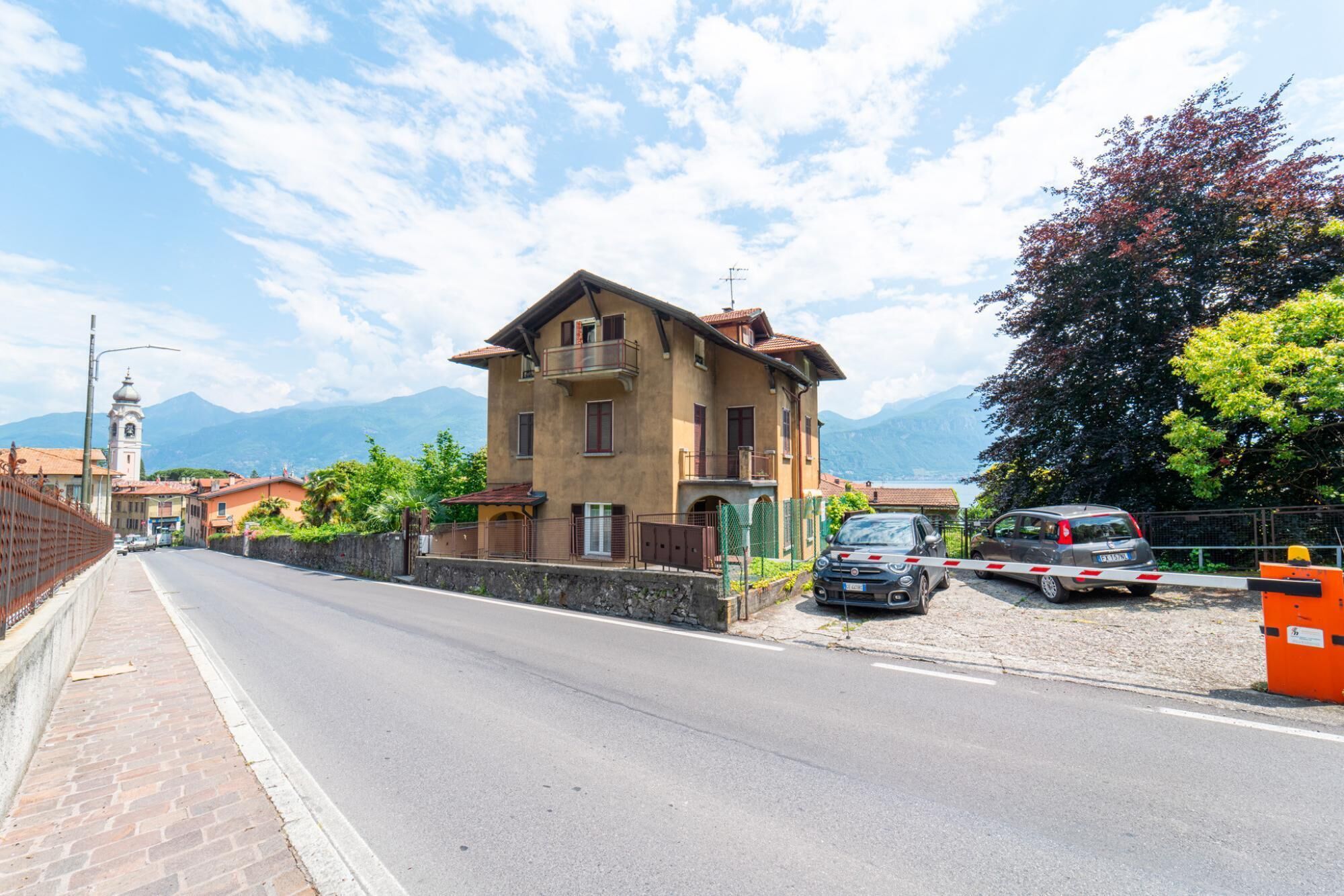 Ein zweistöckiges Gebäude mit Balkon, einer gepflasterten Straße und einem Berg im Hintergrund.