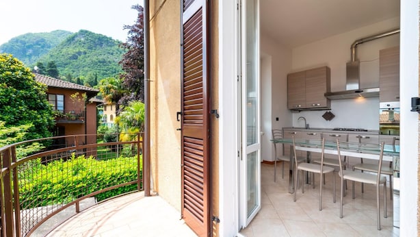 Une cuisine moderne avec une table et des chaises en verre, un balcon doté d’une rambarde en métal et une vue sur un paysage verdoyant.