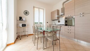 Une cuisine moderne avec une table à manger en verre, des chaises en métal, un four à micro-ondes et des appareils électroménagers en acier inoxydable.