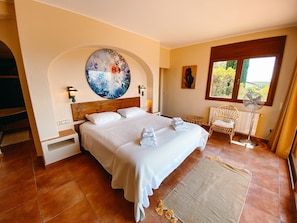 A bedroom with a large bed, a round painting, a chair, and a window. - Villa 'Tres Olivos - Begur' with Mountain View, Wi-Fi and Air Conditioning (Begur)
