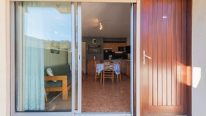 Puerta corrediza de vidrio que da a un comedor con mesa y sillas, una cocina al fondo y una puerta de madera a la derecha.