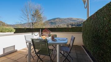 A patio with a table set for two, chairs, a street lamp, and a view of hills.