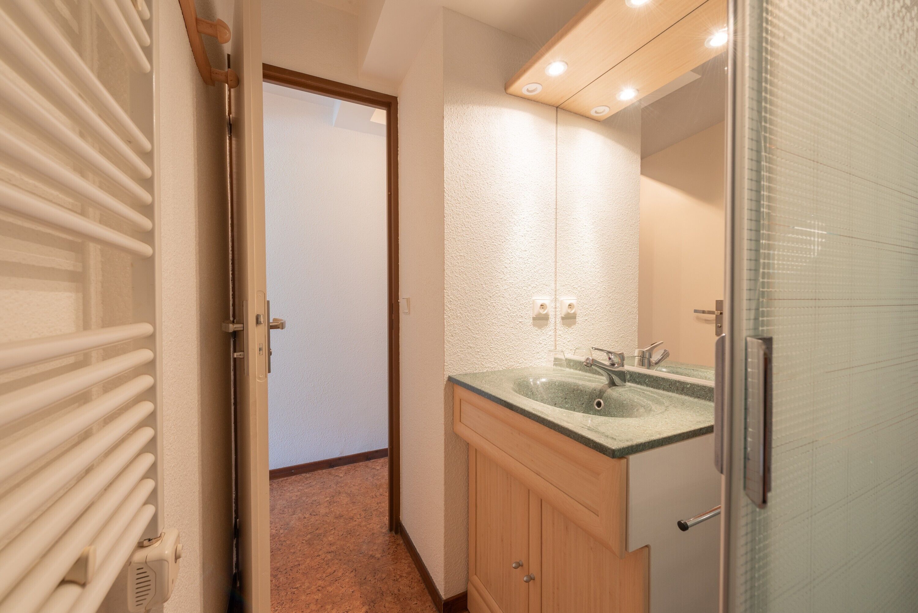A bathroom with a glass shower enclosure, a sink with a granite countertop, and wooden cabinets.
