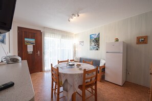 Une cuisine de taille réduite comprenant une table à manger, des chaises, un réfrigérateur et un téléviseur.