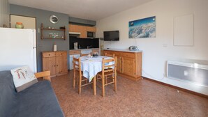 Un espacio habitable compacto con kitchenette, comedor y televisor montado en la pared.