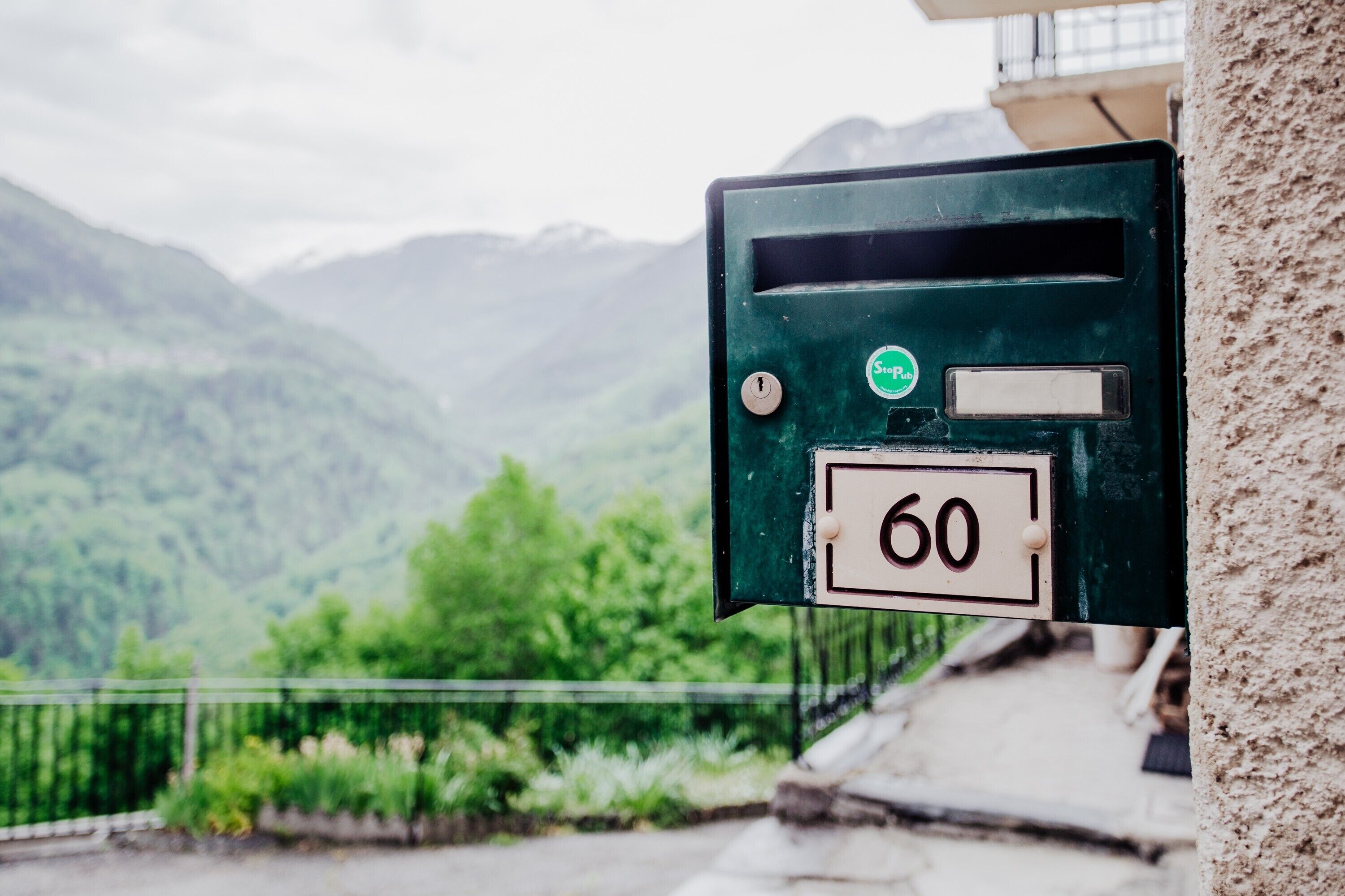 A green utility box with a number '60' on it, set against a backdrop of a mountainous landscape.